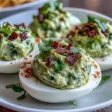 Vibrant deviled eggs filled with zesty guacamole, combining egg yolks, ripe avocado, and a hint of spice for a crowd-pleasing appetizer.