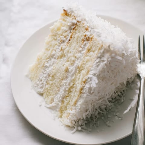 Classic Coconut Cake with fluffy meringue frosting, served on a white platter.