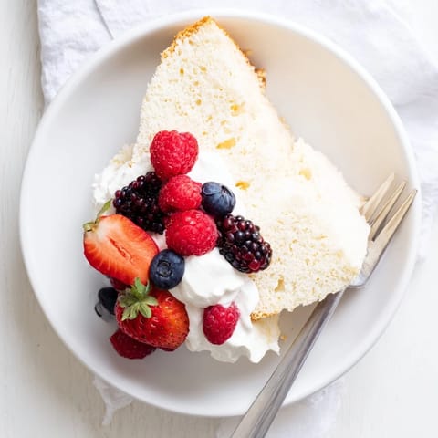 Sliced angel food cake reveals its delicate, fluffy crumb on a white plate, ready for a summer dessert.