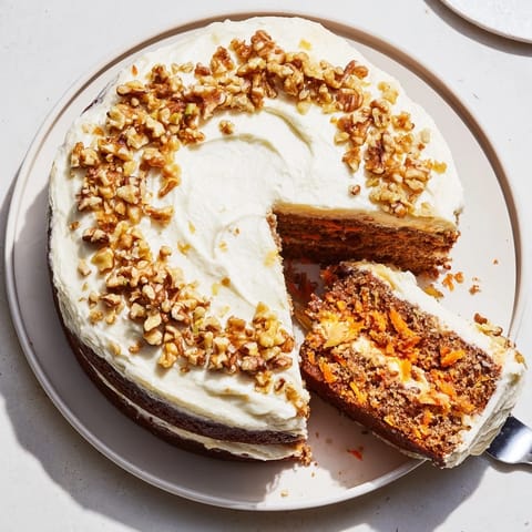 Slice of classic carrot cake with cream cheese frosting and toasted walnuts on a white plate, perfect for a cozy dessert spread.