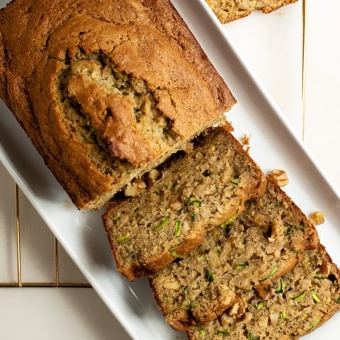 Freshly baked Zucchini Bread cooling on a wire rack, with warm steam rising from the tender, nut-filled slices.