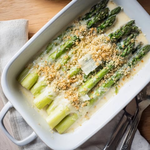A close-up view of a baked asparagus casserole with melted Gruyère and a crunchy breadcrumb topping, ready to be served.