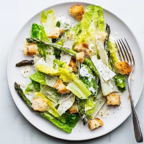 A close-up view of a fresh Roasted Asparagus Caesar Salad featuring charred green spears, creamy white dressing, and shaved Parmesan cheese.