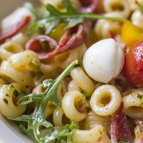 Vibrant Spring Antipasto Pasta Salad showcases ditalini pasta tossed with peppery arugula, salami, mozzarella pearls, and tangy pickled vegetables in a zesty dressing.