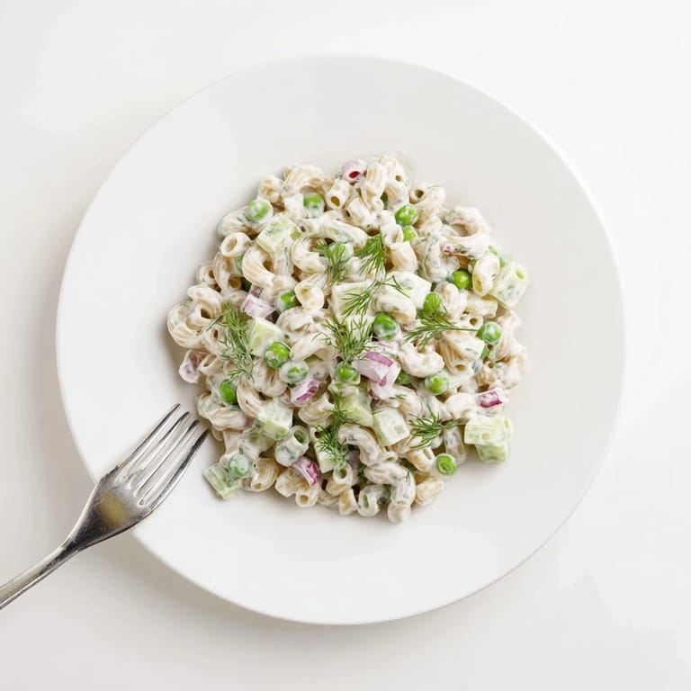 Close-up of creamy dill pickle pasta salad tossed with peas and celery, garnished with fresh dill for a bright, tangy finish.