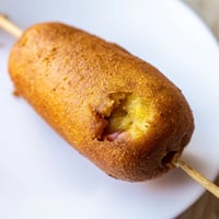 Golden-brown Corn Dogs on sticks, ready to serve with ketchup and mustard on a striped napkin.