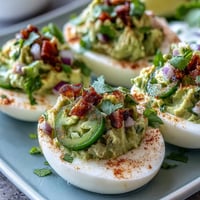 Creamy guacamole stuffed deviled eggs with fresh avocado, lime, and jalapeño, topped with smoked paprika and cilantro.